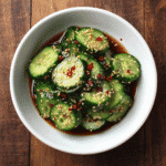 Sliced cucumbers in a white bowl with soy chili dressing and sesame seeds